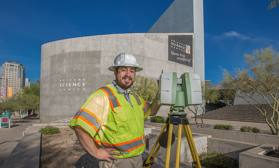 A construction surveyor standing with his equipment in front of the Science Center.