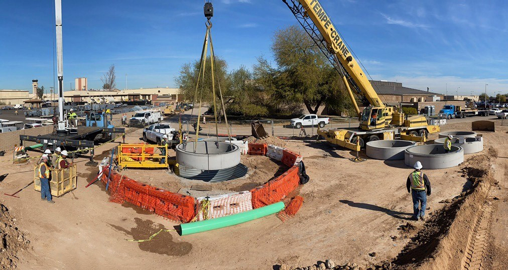 A crane lowering a sewer pipe into the ground.