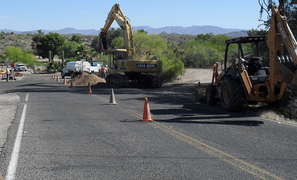 A backhoe (aka digger) working in a 2-lane road.