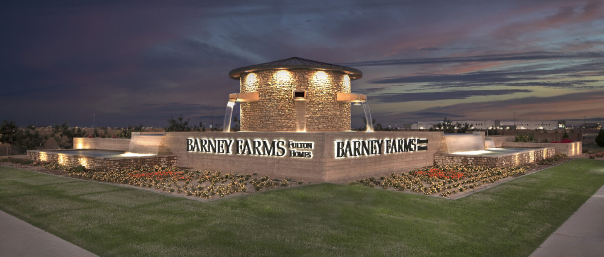 Photo of the Barney Farms entry monument, which is a stone silo with fountain spouts. There are flowers planted in front along with green grass.