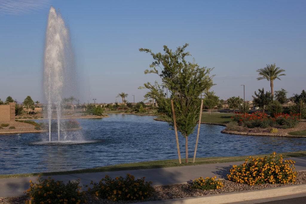 Photo of the lake with a water feature. A sidewalk path circles the lake.